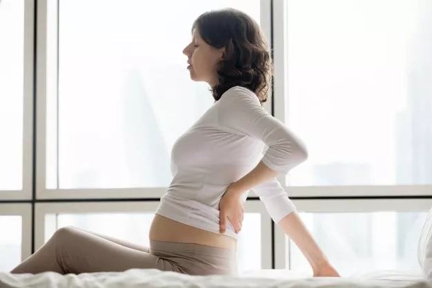 A pregnant woman with a backache and resting on the bed.
