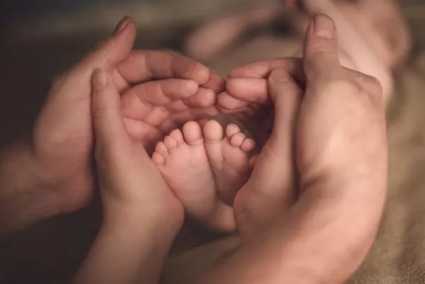 Father and mother holding the feet of their baby and forming a heart shape.