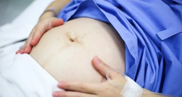 Pregnant woman in hospital garment and experiencing contractions.