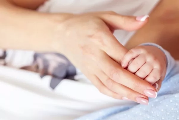 Mother holding onto the hands of her newborn baby. 