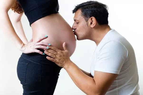 Husband lightly kissing the pregnant belly of his wife