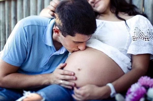 Husband lightly kissing the belly of his pregnant wife