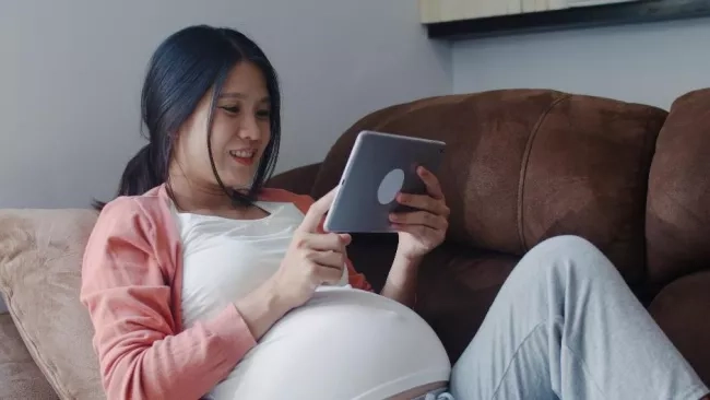 Pregnant mother sitting on the couch looking at maternity plans on her ipad