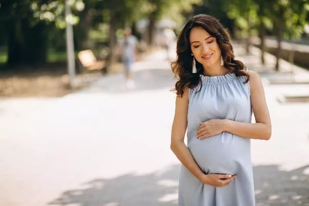 Pregnant mum holding her belly and happily walking outdoors