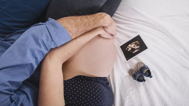 husband hugging pregnant wife and lying on the bed