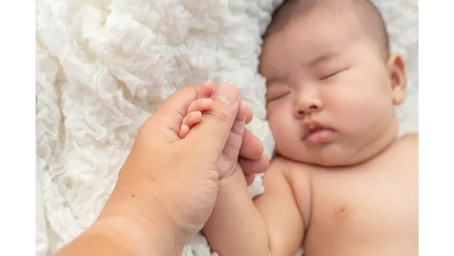 mother lightly holding the hands of her baby