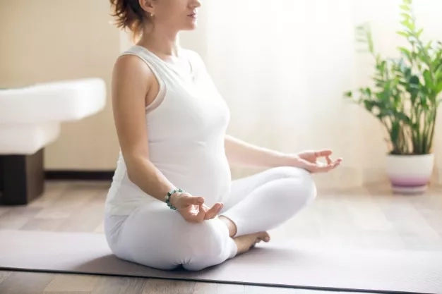 pregnant woman meditating on her yoga mat